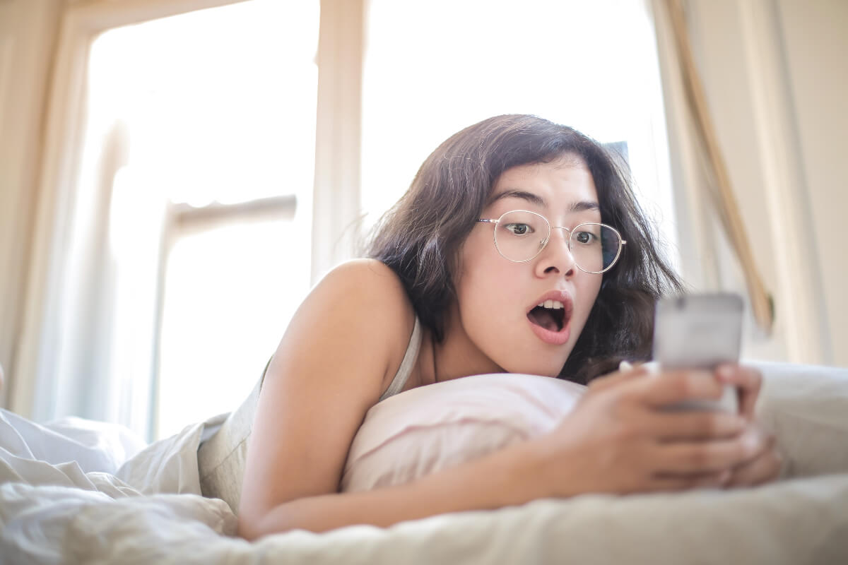 Femme dans son lit avec smartphone, étonnée de découvrir de l'illimité sur réseau d'Orange à moins de 6€ grâce à YouPrice